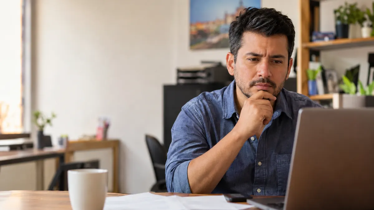 Dueño de un pequeño negocio colombiano revisando pensativo una cotización de servicios digitales frente a su laptop
