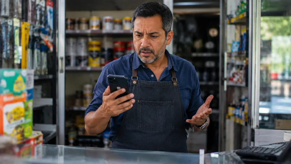 Dueño de negocio detrás de su mostrador mirando el celular sin saber de dónde vienen sus clientes