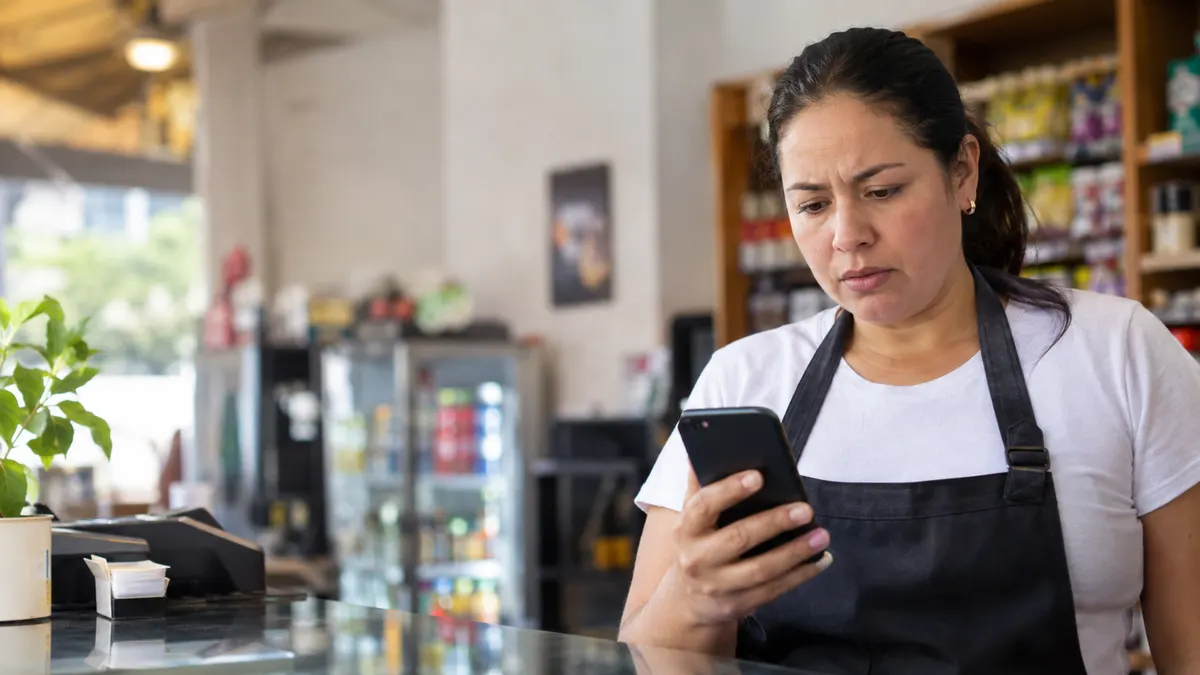 Dueña de un pequeño negocio colombiano revisando preocupada mensajes de WhatsApp sin responder detrás del mostrador de su local
