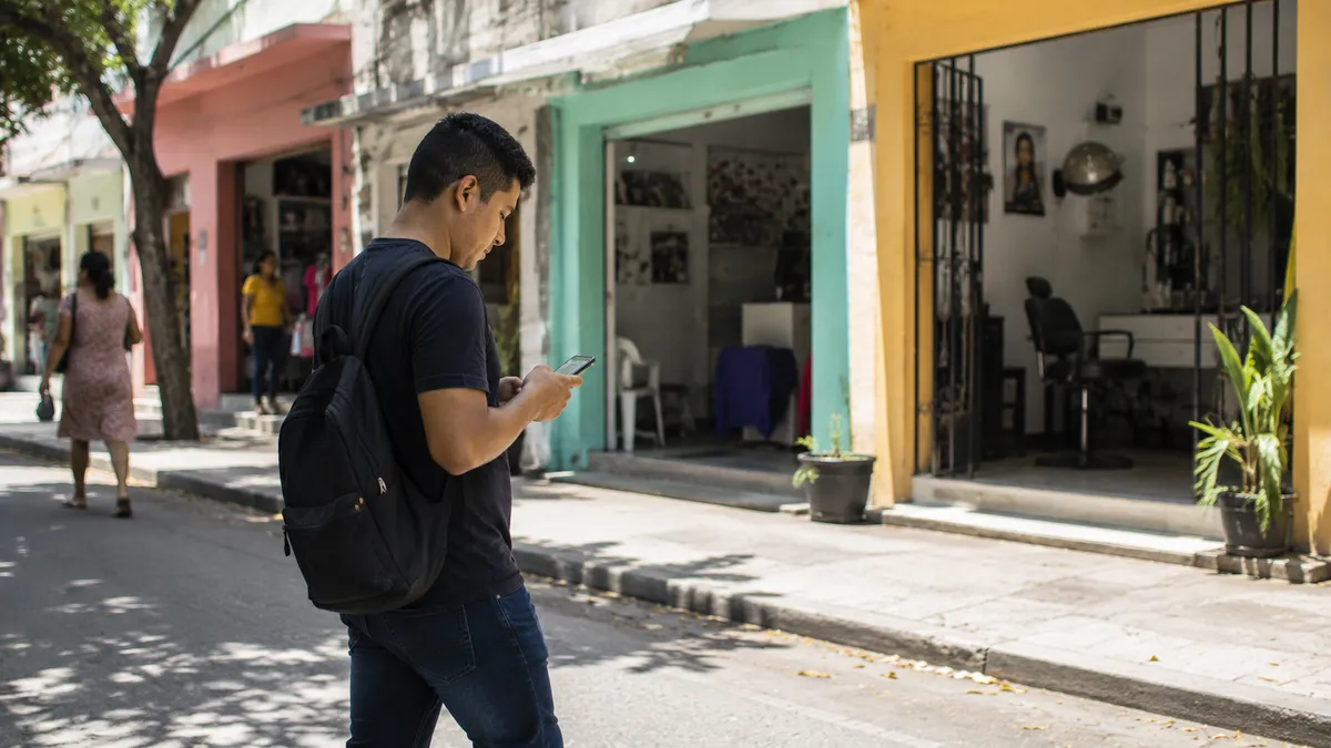 Persona buscando un negocio en su celular mientras camina por una calle comercial en Barranquilla